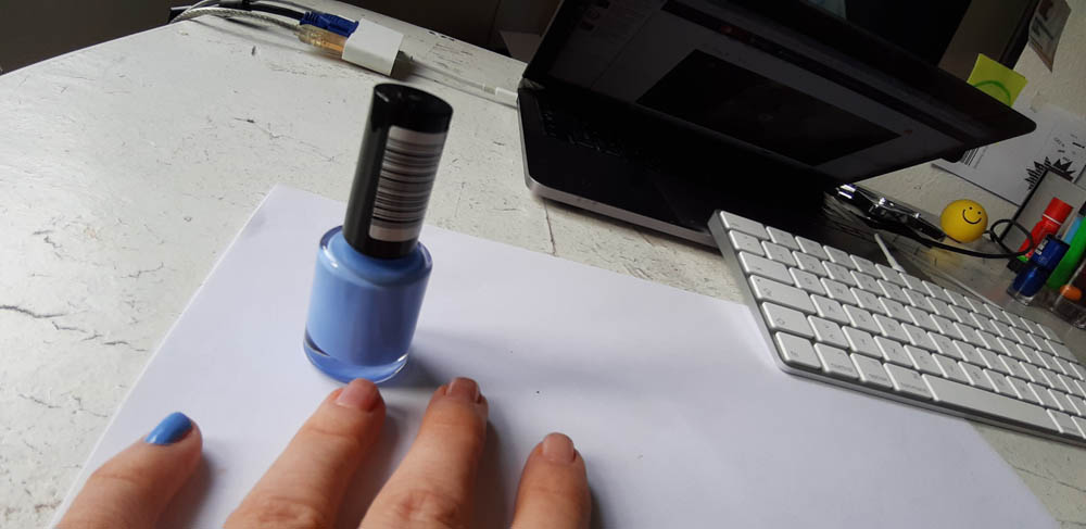 Foto-Beispiel zum Starterkit ein Stück Himmel. Das Foto zeigt eine Hand mit pastellfarbenem Nagellack. Es ist ein Blauton. Zuckerwattenblau. Die Nagellackflasche steht daneben. Der Blick fällt auf einen Schreibtisch mit einem Laptop und einer Tastatur. Die Hand stützt sich auf den Tisch.
