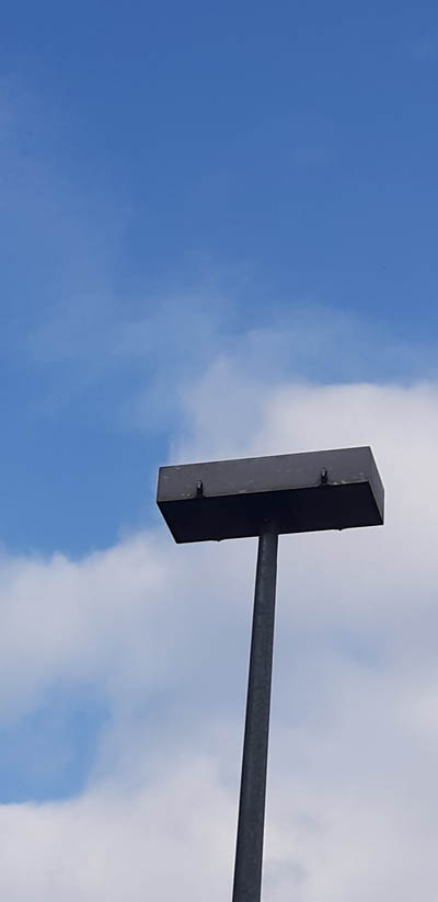 Beispiel-Foto zum Startkit #gesichtersindüberall. Ein Lampenkonstruktion an einer Bahnhaltestelle. In extremer Aufsicht fotografiert. 2 Schrauben schauen wie zwei Augen nach unten.