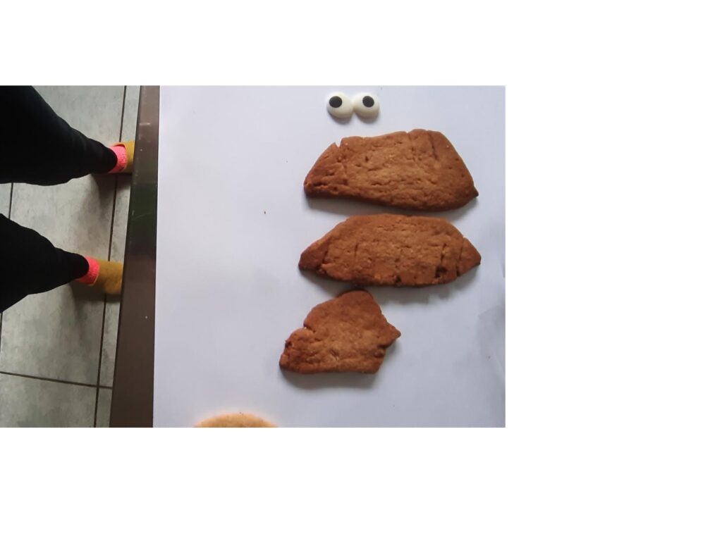 Fotobeispiel zum Startkit Wolke oder Keks. Ein Wesen aus drei Keksen  schaut vom Backblech. Fotografiert aus der Vogelperspektive. Die Füße und neonrosafarbenen Socken sind zu sehen. 