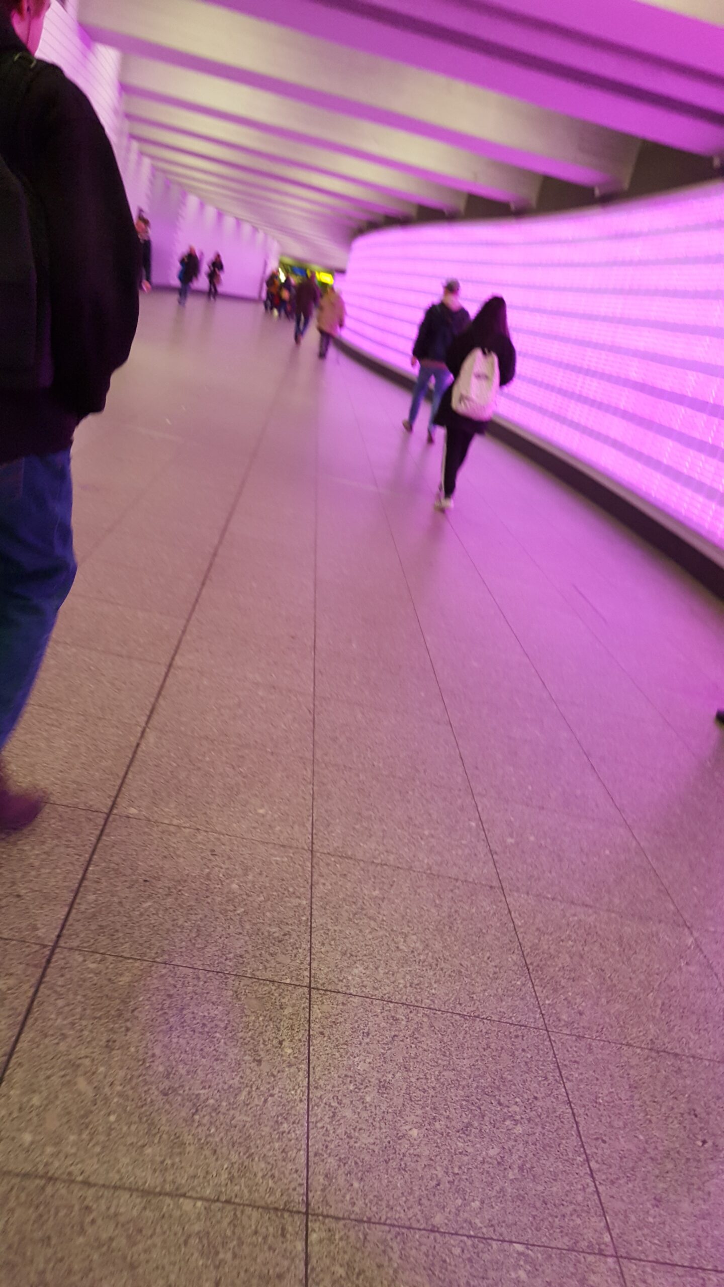 Beispiel-Foto zum Thema #Handy-Malerei. Eine Unterführung ist in rosafarbenes Licht getaucht. Eine Person mit weißem Rücksack geht wie viele weitere Menschen ihren Weg. 