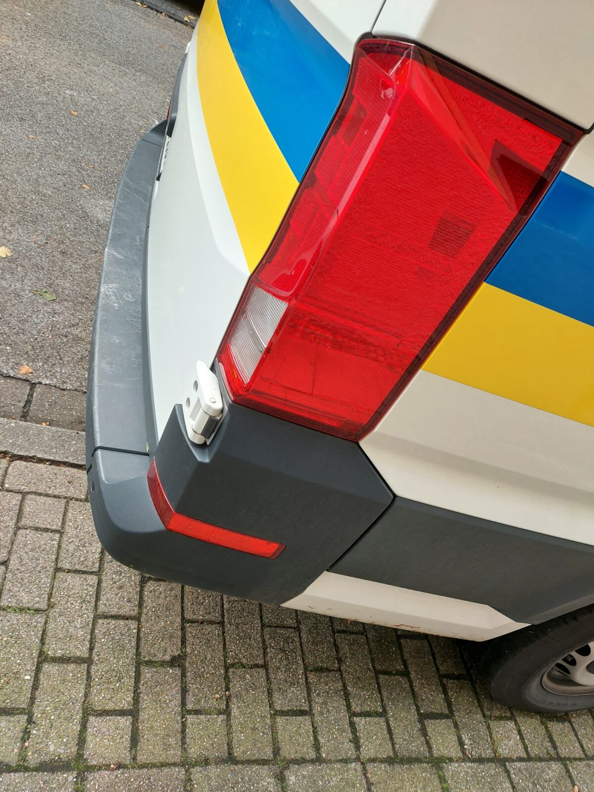 Beispiel-Foto zum Thema #Handy-Malerei. Reihe Primärfarben. Zu sehen ist. Das rote Rücklicht eines weißen Lieferwagens in Kombination mit dem Firmenlogo. Einem blauen und einem gelben Streifen.