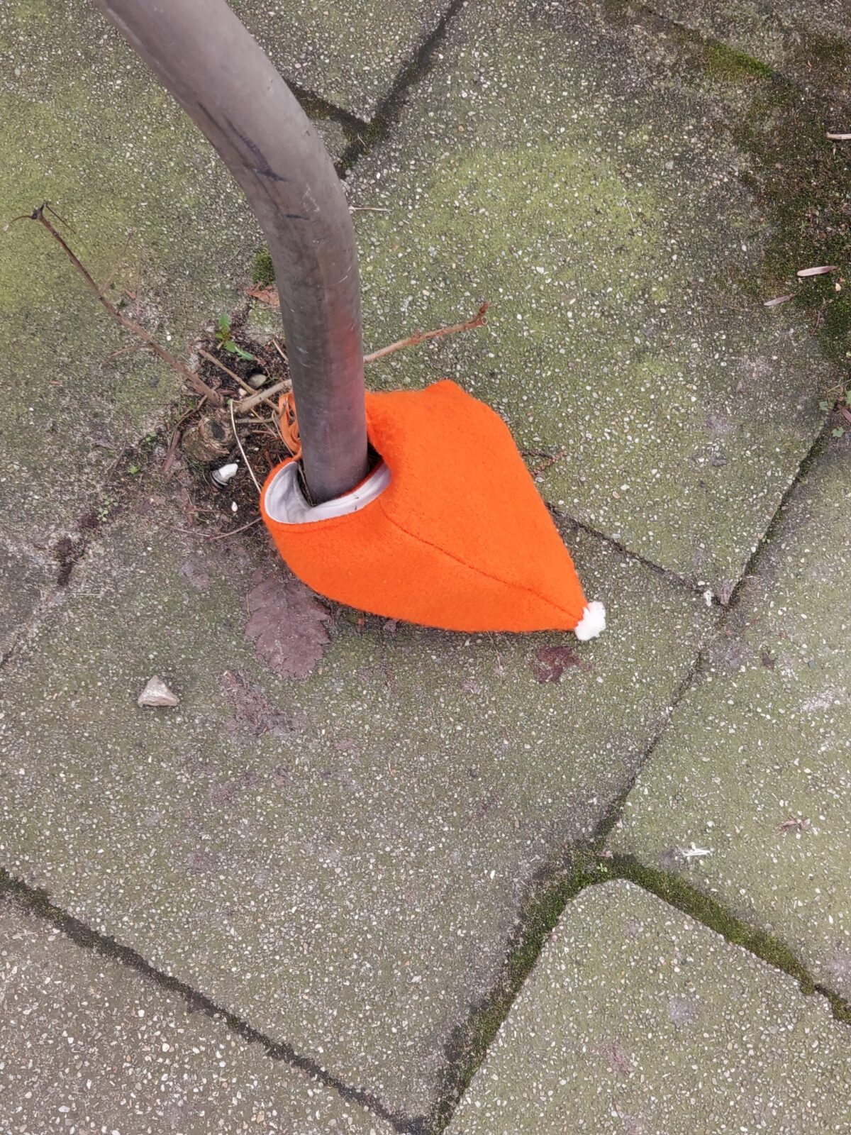 Beispiel-Foto zum Thema Add-one und Add-on. Eine Kindermütze in leuchtendem Orange liegt am Boden und wurde dort  an einem Fahrradständer angebunden. Die Mütze hat einen kleinen weißen Bommel.