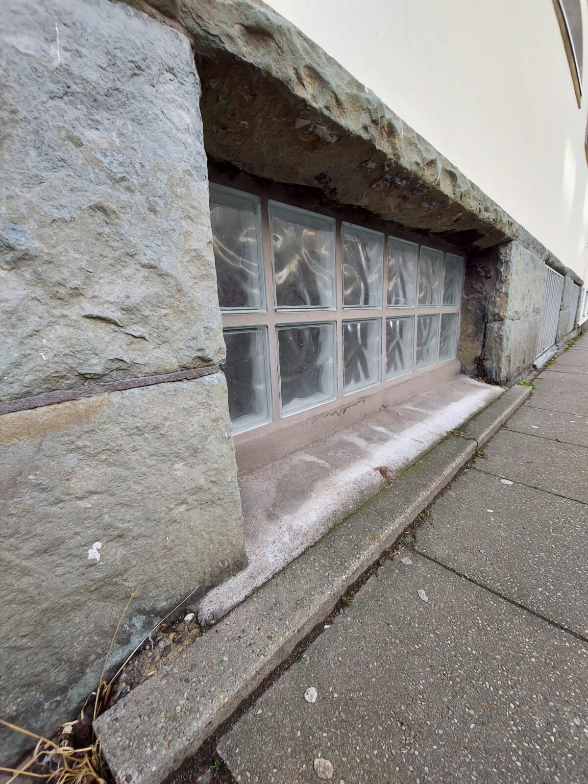 Beispiel-Foto zum Thema "Little Stages" im Stadtraum, ein Fenster im Souterrain, mit weißen Glasbausteinen, verkleidet mit Sandsteinplatten