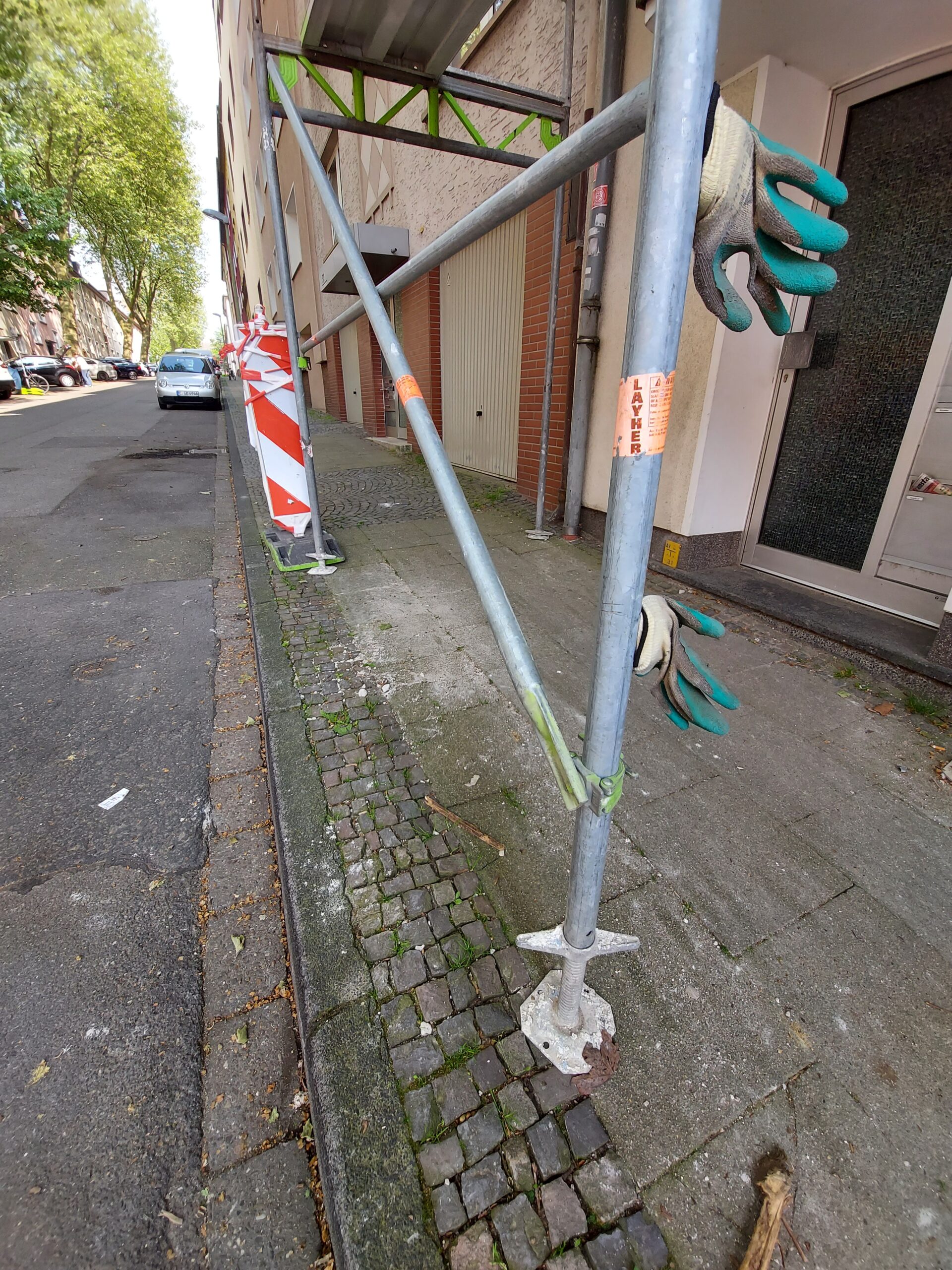 Beispiel-Foto, das Prinzip "And-on(e) im Stadtraum, 2 grüne Arbeitshandschuhe aufgesteckt an einem Baugerüst