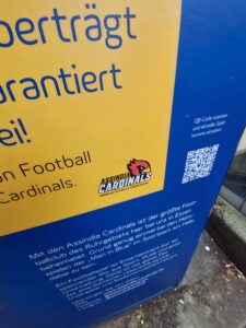 Beispiel-Foto zum Starterkit  #cityzoo. Das Logo eines Football-Vereins ist in der Ecke eines gelben Plakates mit blauer Schrift und blauem Rahmen zu sehen. Das Logo besteht aus einer roten Vogel-Figur und einem Schriftzug.