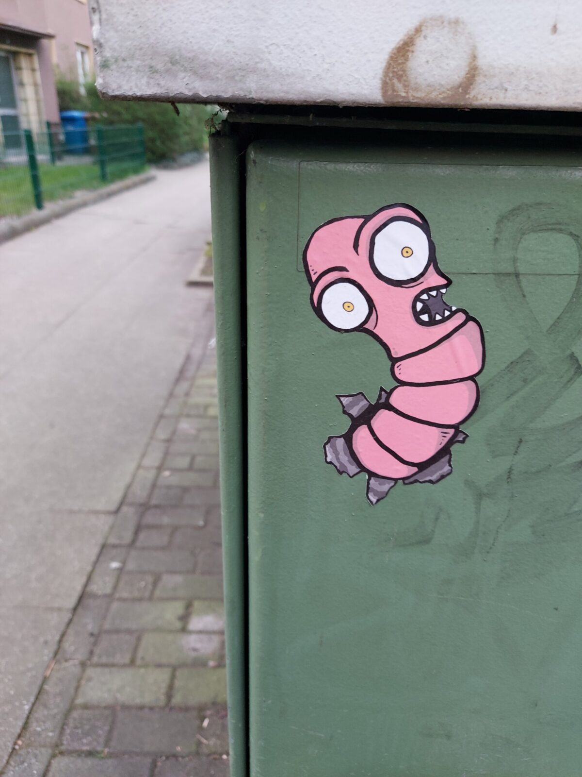 Beispiel-Foto zum Thema #cityzoo. Graffiti auf einer grünen Mülltonnenbox, zu sehen ist ein rosafarbener Wurm mit weit aufgerissenen Augen