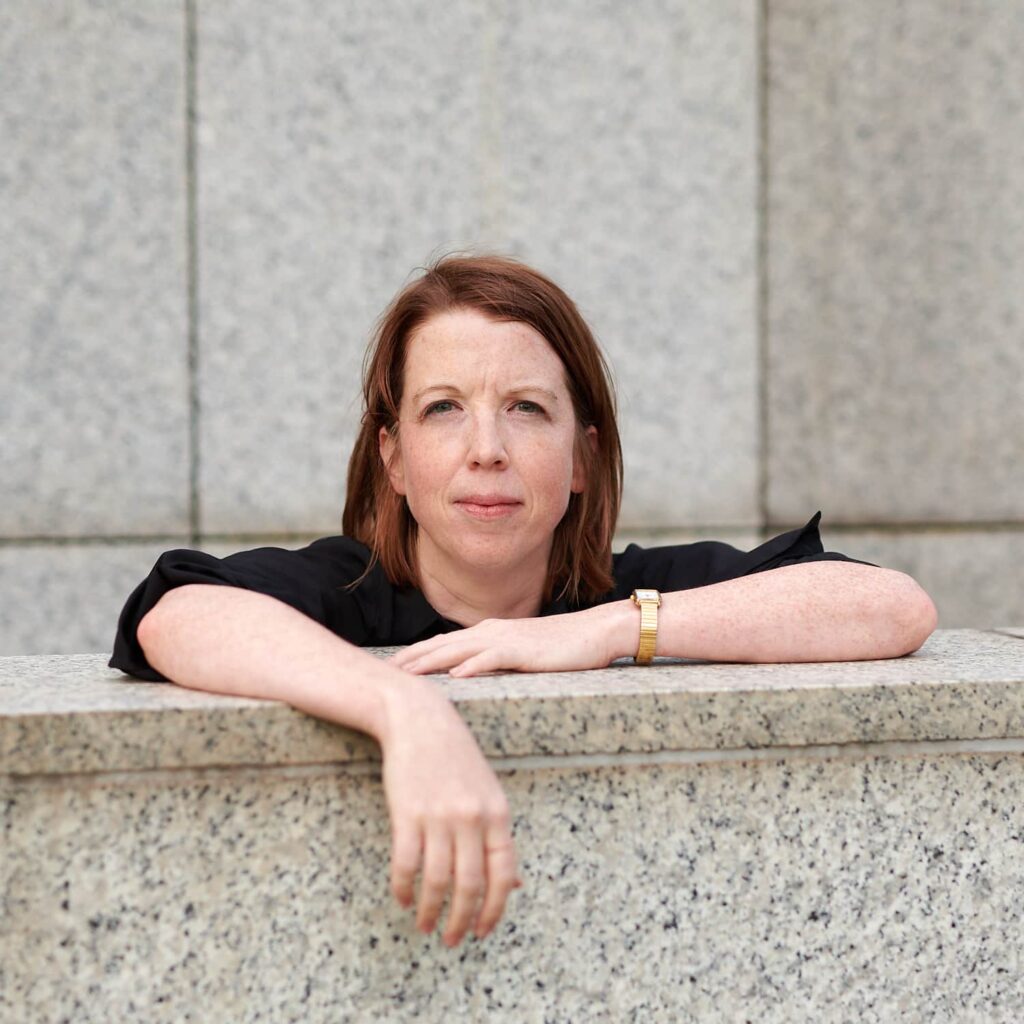 Portrait Dr. Sabine Sutter. Sabine Sutter hat beide Arme auf einer Mauer abgelegt. Die rechte Hand hängt locker über der Kante. Sabine Sutter trägt eine schwarze Bluse deren Ärmel bis zum Ellenbogen hochgekrempelt sind.