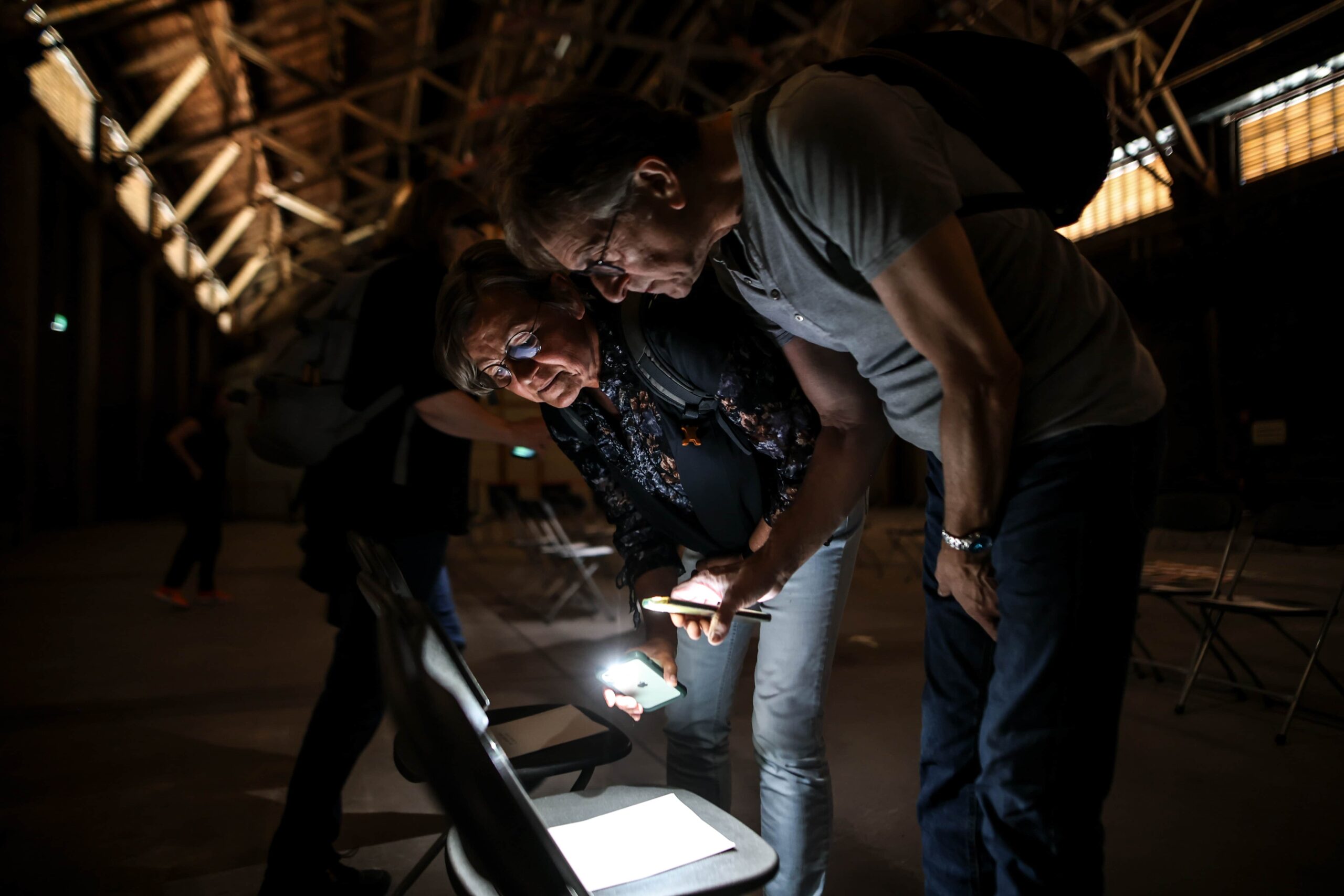 Zusammen ins Denken kommen durch Kunst. Startsituation im Workshop "Du und D-eine Gegenwart". Maßkonzeption von STUDIO WUNDERMATERIAL für die Stiftung Zollverein Essen.Zwei Personen leuchten mit ihren Handytaschenlampen auf einen Zettel. Der räum ist Dunkel im Hintergrund ist eine weitere Person zu sehen.